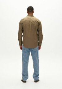 Olivenfarbendes Langarmhemd mit Button-Down-Kragen, kombiniert mit lässigen, hellblauen Jeans und schwarzen Schuhen, von hinten betrachtet.