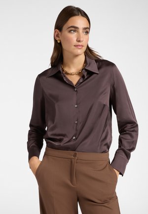 Camicia button-up in satin marrone con colletto e maniche lunghe, abbinata a pantaloni marroni. La camicia presenta una texture liscia e una vestibilità rilassata.