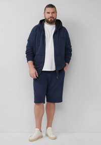 Navy Zip-Hoodie- und Shorts-Set, mit einem weißen T-Shirt darunter und weißen Sneakers. Glatter Stoff mit einer lässigen Passform und dezenten Details.