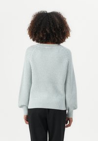 Svetlo modra pletena pulover s teksturiranim vzorcem, raglan rokavi in riban rob, kombiniran s črnimi hlačami. Prikazan je zadnji pogled.