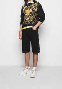 Black sweatshirt with colorful floral embroidery, paired with black knee-length shorts and white chunky sneakers with yellow accents.