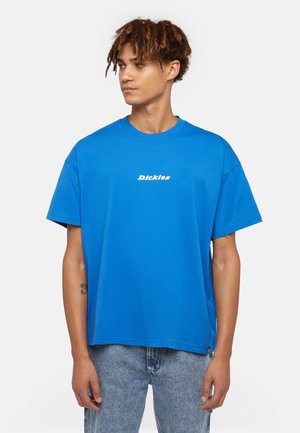 Camiseta de algodón azul con cuello redondo y mangas cortas. Presenta un logo blanco en el pecho y un dobladillo recto. Se combina con unos vaqueros de denim claros.