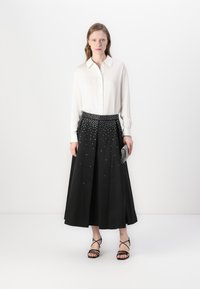 Fehér hosszúujjú ing, fekete midi szoknya ezüst szegecsekkel díszítve, fekete pántos szandállal és fémes clutch táskával párosítva.