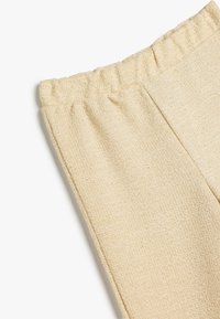 Lys beige, strukturerede bukser med elastisk talje. Stoffet fremstår blødt og strikket med et subtilt vævet mønster.
