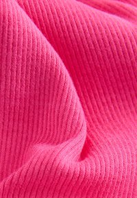 Texturerat ribbat tyg i stark rosa. Mjukt, stretchigt material med växelvis upphöjda och nedsänkta ränder som skapar en vågliknande effekt.