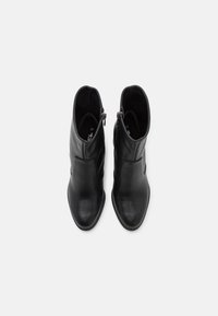 Paire de bottines en cuir noir avec fermetures éclair latérales, vue de dessus sur un fond clair uni.