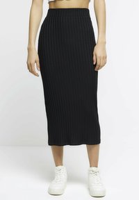Czarna, prążkowana midi spódnica z elastycznym paskiem w talii i dopasowanym krojem, zestawiona z białymi, wysokimi trampkami.