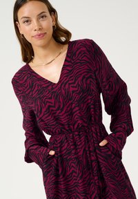 Burgundy dress with black zebra stripes, V-neck, long sleeves, and a drawstring waist. Features side pockets and a soft texture.