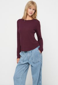 Mørkerød langærmet top i ribbet stof, parret med løse lys blå denimbukser med sidelommer og en afslappet pasform.