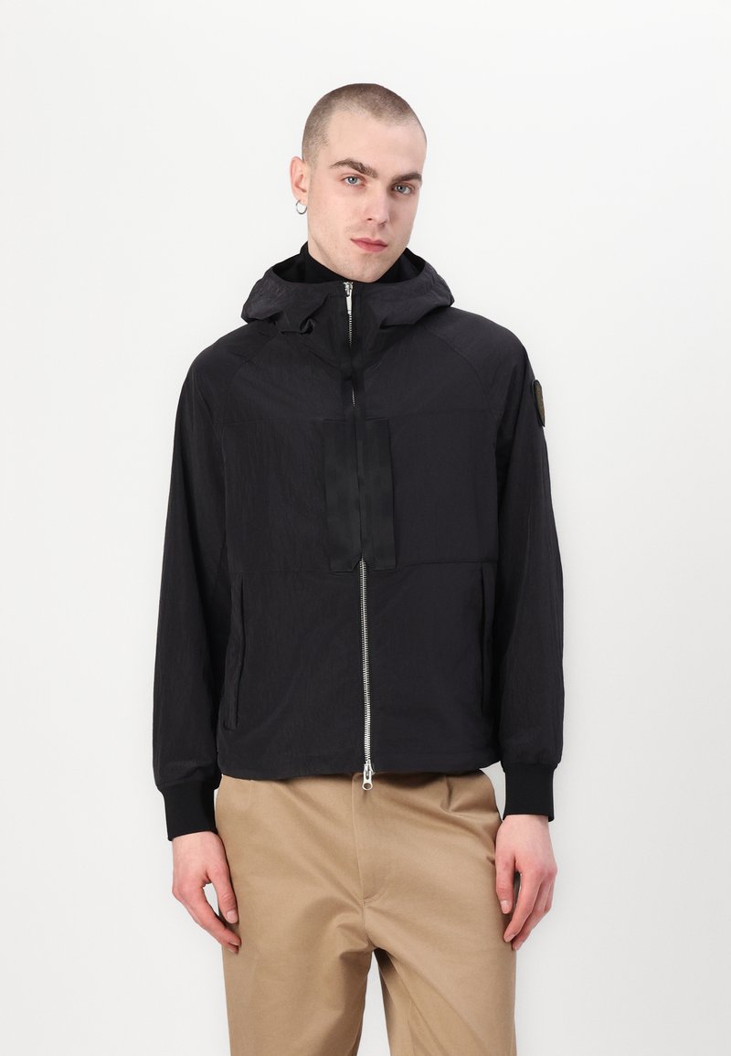 Black lightweight jacket with a zip front, hood, and chest pocket. Features elastic cuffs and a textured fabric for a sleek appearance.