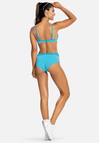 Niebieski i biały bikini w paski z regulowanymi ramiączkami, wysokim stanem i gładkiego, elastycznego materiału. Modelka widziana z tyłu.