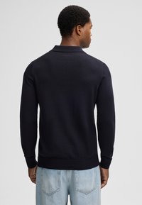 Marineblauer Strickpullover mit Kragen, strukturiertem Stoff und gerippten Bündchen und Saum. Ansicht von hinten, Model trägt hellblaue Jeans.