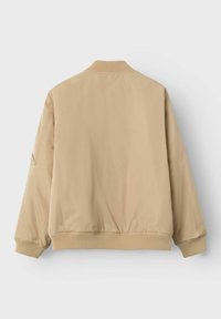 Beige bombers jaka ar ribotu apkakli un piedurknēm, kas izceļas ar gludu tekstūru un elastīgu jostu, veidota, lai nodrošinātu brīvu piegriezumu.