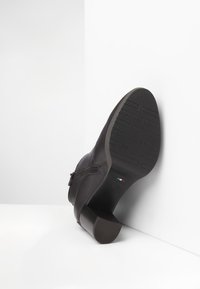 Black leather ankle boot with a low block heel, side zipper, textured rubber sole, and small Italian flag detail.