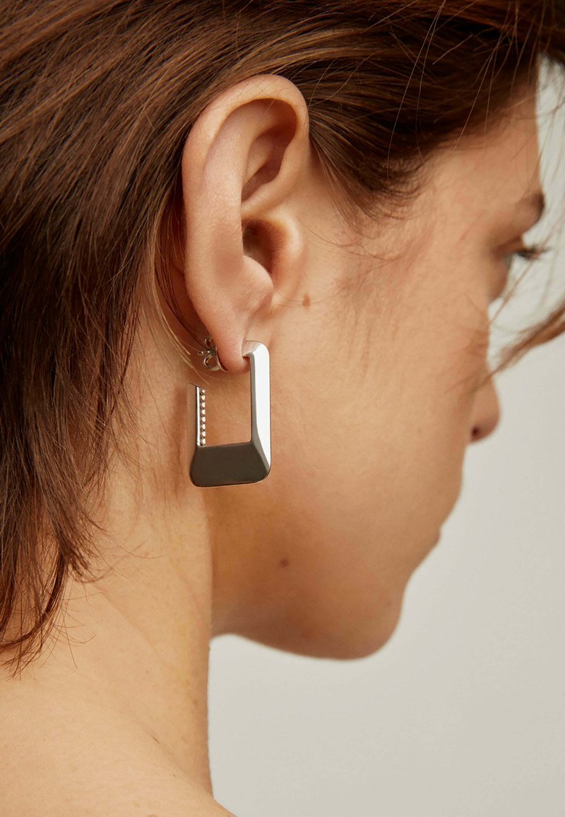 Pendientes de plata geométricos con un diseño angular y abierto, con un acento texturizado. Acabado suave y superficie metálica brillante.