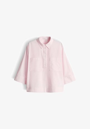 Chemise rose pâle surdimensionnée avec manches trois-quarts, deux poches avant, patte de boutonnage et col classique sur fond blanc.