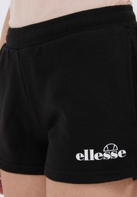 Pantalones cortos de algodón negros con cintura elástica, que cuentan con bolsillos laterales y un logotipo blanco de "ellesse" impreso en la parte inferior de la pierna.