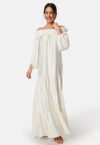 Off-the-shoulder creme maxi kjole med flæsekant ved halsen, lange ærmer og tierede stofpaneler, lavet af blødt, let materiale.