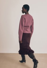 Plum pulover z okroglim izrezom, v kombinaciji s rjavim puhastim krilom s frufrum na robu in črnimi škornji s koničastim nosom do kolen.