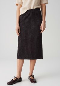 Gonna midi nera a costine con vita elastica, caratterizzata da un tessuto testurizzato. Abbinata a scarpe in pelle scura, che presentano un design semplice.