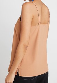 Persikofärgad, ärmlös topp med tunna band, lös passform och en slät yta. Har en sidoklyvning för extra ventilation.