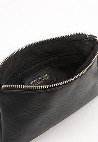 Svart läderpung med en guldfärgad dragkedja. Har en innerficka och en etikett med texten "VERO MODA COLLECTION" i guld.