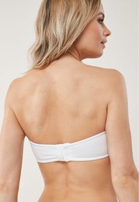 Balta strapless bikini augšdaļa, izgatavota no gludas auduma, ar bezšuvju dizainu un aizmugures aizdari, lai nodrošinātu drošu piegulšanu.