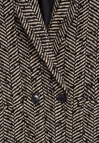 Blazer à double boutonnage avec un motif chevron noir et beige, doté de deux boutons noirs et d'un revers cranté.