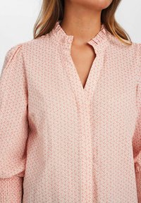 Blusa rosa chiaro con motivo floreale, collo arruffato e maniche lunghe a palloncino con dettagli smock. Design a scollo a V.