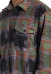 Groene, zwarte, paarse en oranje geblokte fleece shirt met drukknoopjes en een voorzak met een knoopflap.