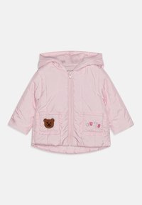 Pink quilted jacket with a hood, featuring a bear appliqué on one pocket and "GUESS" embroidered on the other. Soft fabric with zip closure.
