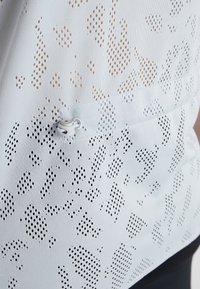 Tessuto sportivo azzurro chiaro con design a rete caratterizzato da fori di diverse dimensioni, con un piccolo gancio per cordoncino bianco incorporato nella cucitura.