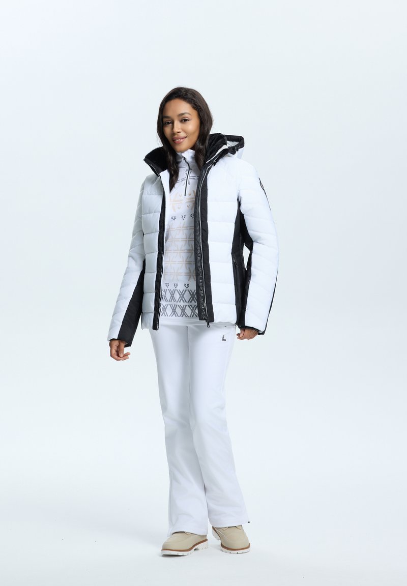 Witte pufferjack met zwarte accenten, ritssluiting aan de voorkant en een capuchon. Gevoerde witte basislaag en witte sneeuwbroek maken de outfit compleet.