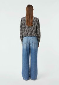 Schwarz-weiße gemusterte Langarmbluse kombiniert mit hochgeschnittenen, weit geschnittenen hellblauen Jeans, die eine entspannte Passform und ein lässiges Design präsentieren.