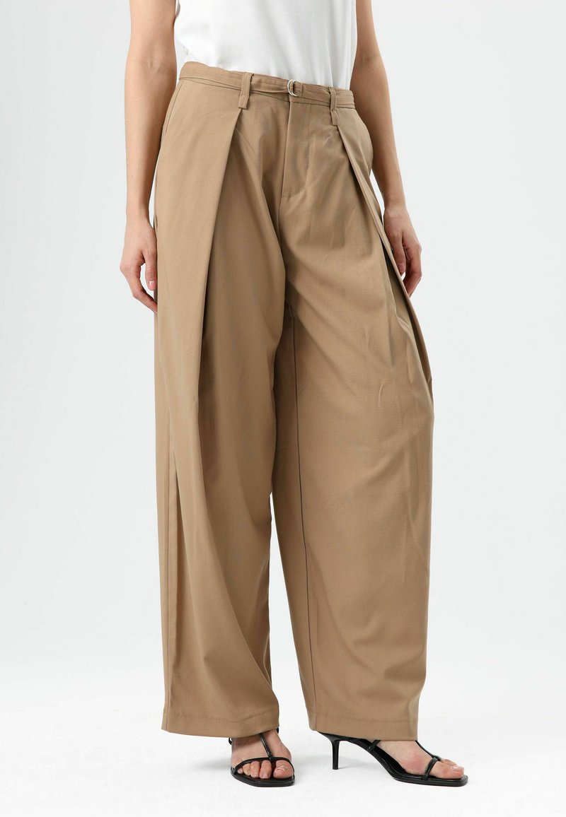 Tan wide-leg trousers with pleated details, made from lightweight fabric. Features a belted waist and falls to the floor, styled with black heels.