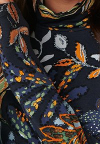 Nära vy av en person som bär ett mörkt plagg med blommönster i orange, gröna och vita bladmotiv.