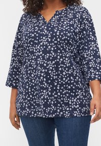 Top blu navy con scollo a V e maniche a tre quarti, caratterizzato da un motivo floreale bianco in tutto il capo. Tessuto morbido con una vestibilità comoda.