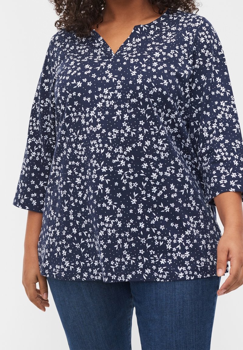 Top blu navy con scollo a V e maniche a tre quarti, caratterizzato da un motivo floreale bianco in tutto il capo. Tessuto morbido con una vestibilità comoda.