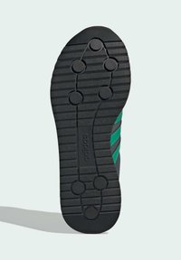 Semelle en caoutchouc noir avec des motifs de traction circulaires, présentant des rayures vertes et noires sur le côté. Surface texturée pour une meilleure adhérence.