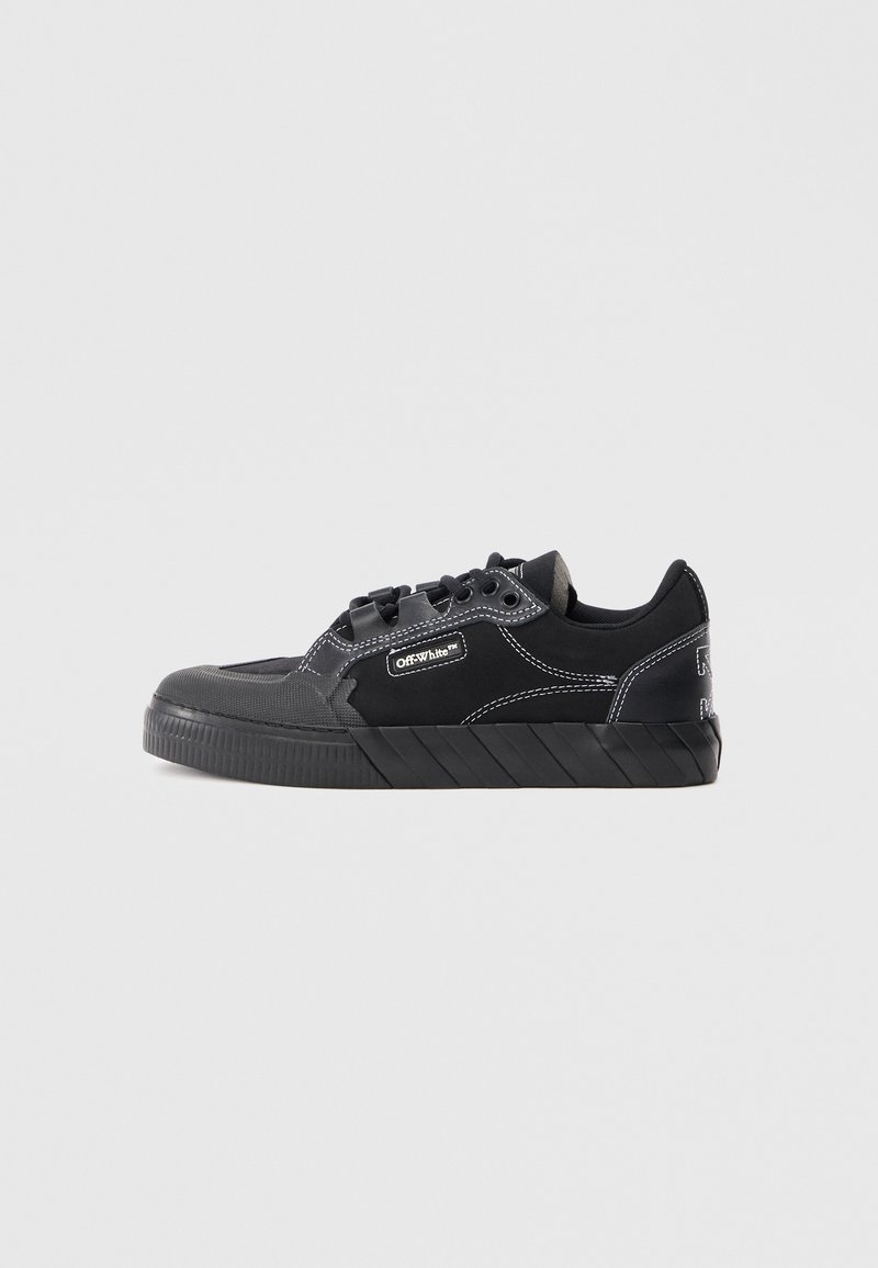 Zapatilla casual negra de caña baja con suela gruesa, costuras blancas y etiqueta "OffWhite" en el lateral, presentada sobre un fondo liso.