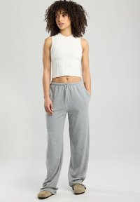 Valkoinen ribattuja lyhyt tanktoppi yhdistettynä vaaleanharmaisiin collegehousuihin. Asusteessa on rento istuvuus ja nyöri vyötäröllä.