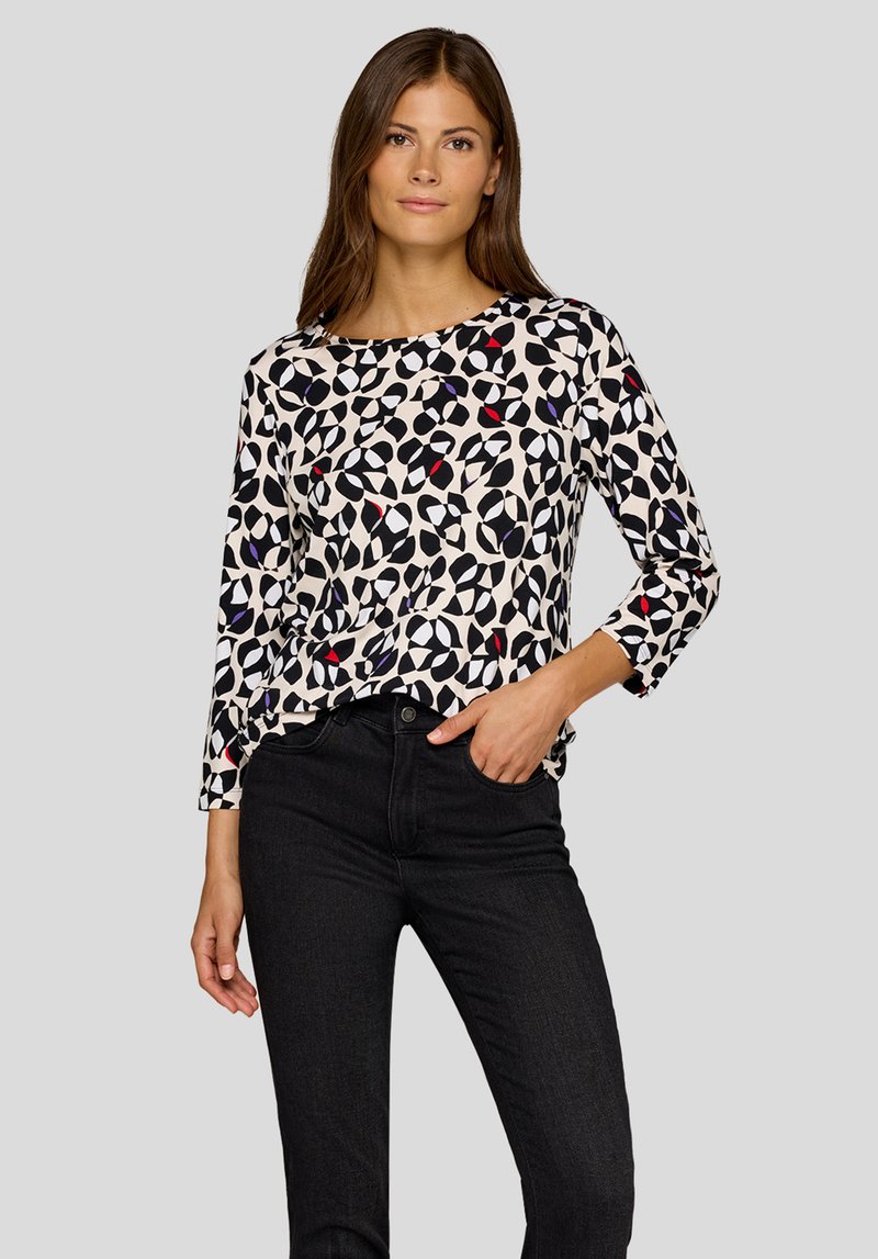 Long-sleeve blouse in cream with black, red, and purple abstract patterns. Soft fabric, loose fit, round neckline, and three-quarter sleeves.