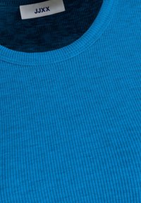 Niebieska, prążkowana tkanina z okrągłym dekoltem. Posiada teksturowaną powierzchnię oraz metkę z napisem "JJXX" blisko kołnierza.