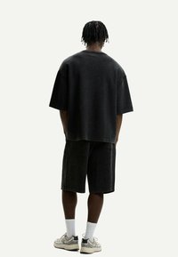 Oversized black cotton crew neck t-shirt and matching shorts. Soft texture, relaxed fit, and minimal stitching detail. Casual footwear with white socks.