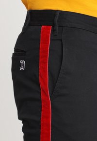 Svarta byxor med en röd sammetssida, med en liten broderad logga på framläggs ficka och en klassisk passform.