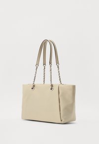 Beige shopper-taske med en glat tekstur, der har dobbelte stofstropper og kædeaccent, udstyret med metaldele ved stroppens forbindelser.