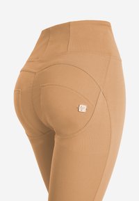 Leggings beige a vita alta con una texture liscia, tasche curvate e un piccolo logo accentato vicino alla tasca posteriore destra.