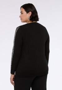 Czarny sweter z dzianiny z długimi rękawami, z srebrnymi paskami wzdłuż ramion i okrągłym dekoltem.