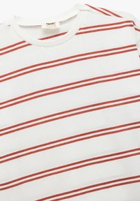 Witte katoenen t-shirt met horizontale rode strepen, ronde halslijn en korte mouwen. Bevat een klein merkje op de kraag.