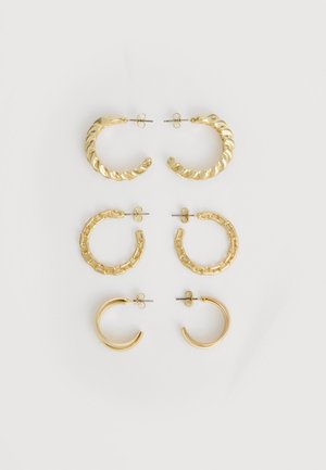 Három pár arany karika fülbevaló különböző textúrákkal – csavart, láncszemes és sima – fehér háttéren, függőlegesen elrendezve.